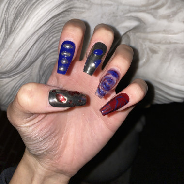 A manicured hand. The fingernails are long and have different nail designs. Some nails are blue, others reddish, adorned with various organic shapes on top.