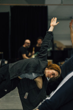 A scene from a Cara Rother workshop. It shows Cara Rother doing a kind of stretching exercise. Cara is dressed in sporty clothes and stretches her left hand in the air. 