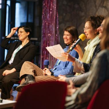   Podium situation: Mónica García Vicente, Selina Glockner and Heike Bröckerhoff can be seen on the podium from left to right. They laugh while Heike speaks to the audience.