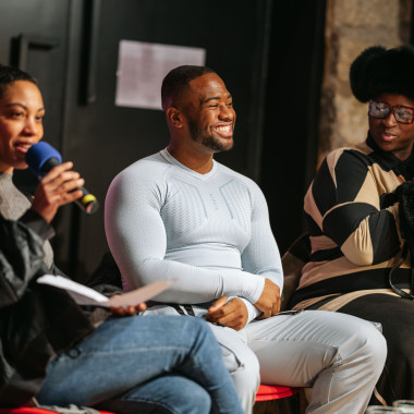 Podium situation, from left to right German Traiblazer Leo, Founding Father Typhoon Angels and Icon Matyouz Tantine Royalty. German Traiblazer Leo speaks into a microphone and looks into the audience. Founding Father Typhoon Angels laughs. 